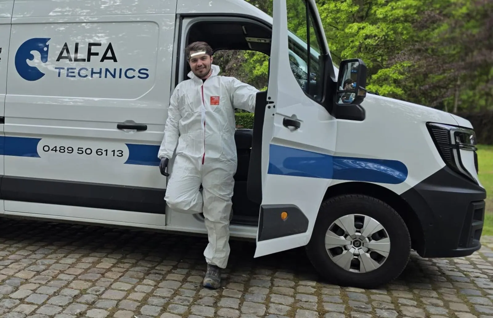 Medewerker van Alfa Technics in werkkledij naast de beletterde bedrijfswagen op een werf