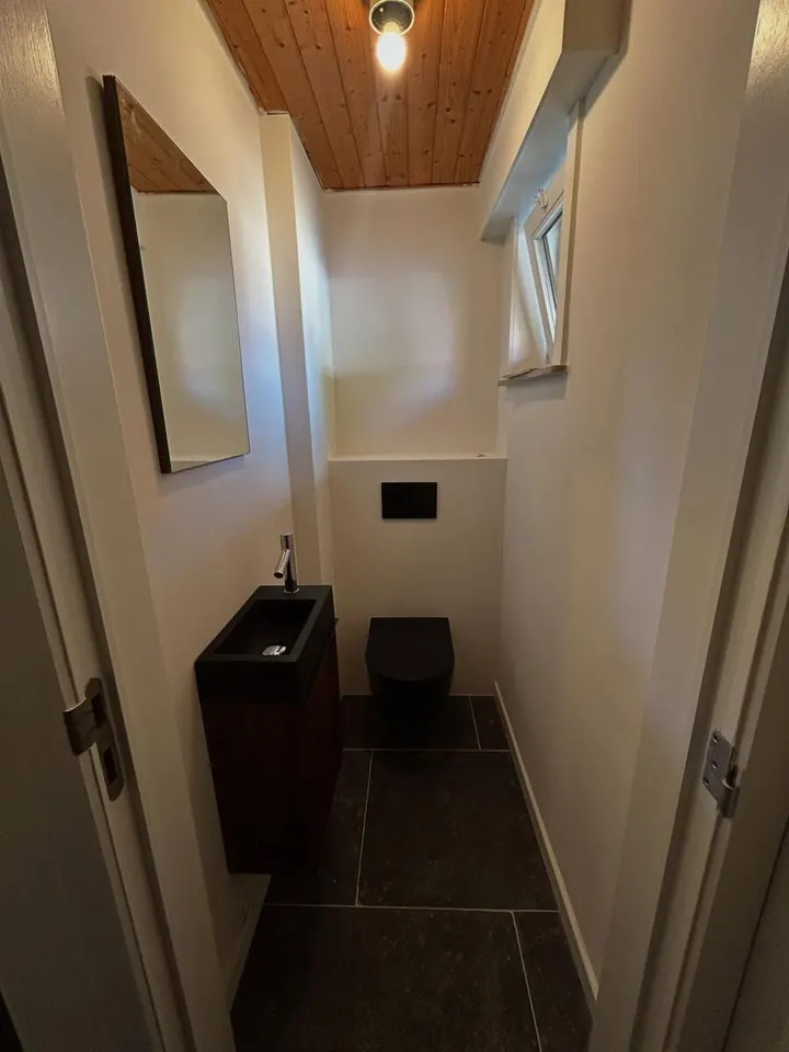 Afgewerkte moderne toiletruimte met zwart hangend toilet en houten plafond